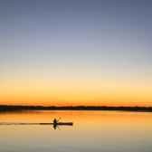 silhouette of man inside of boat sailing on body of water during sunset